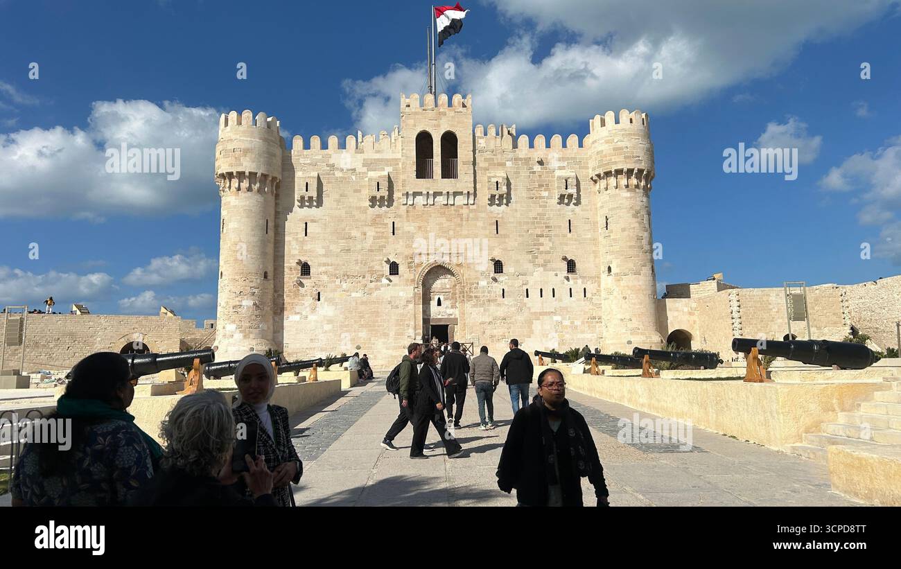 Alexandrie, Égypte - 13 février 2025 : visiteurs à la citadelle médiévale de Qaitbay forteresse avec drapeau égyptien et canons exposés. Banque D'Images