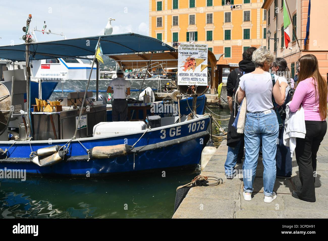 Les gens font la queue sur le front de mer pour acheter de la nourriture à partir d'un bateau de fruits de mer frit dans le petit port, un jour de printemps ensoleillé, Camogli (Gênes), Ligurie, Italie Banque D'Images