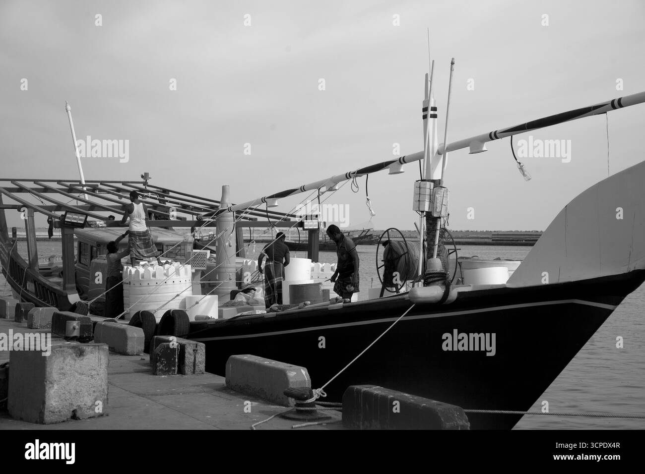 des hommes sur un boutre amarrés au port de sur dhow chargeant des marchandises au sultanat de sur oman Banque D'Images