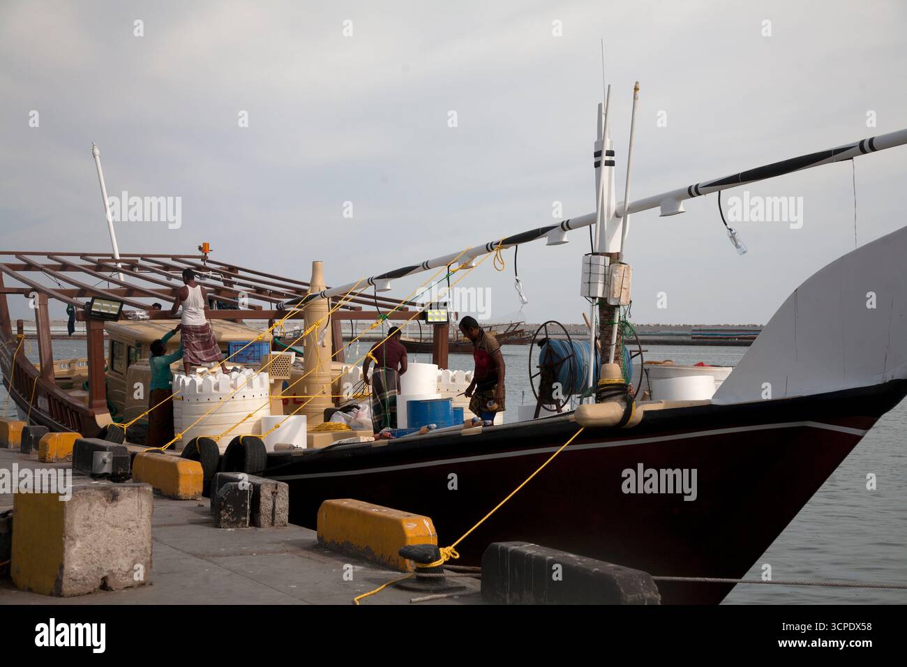 des hommes sur un boutre amarrés au port de sur dhow chargeant des marchandises au sultanat de sur oman Banque D'Images