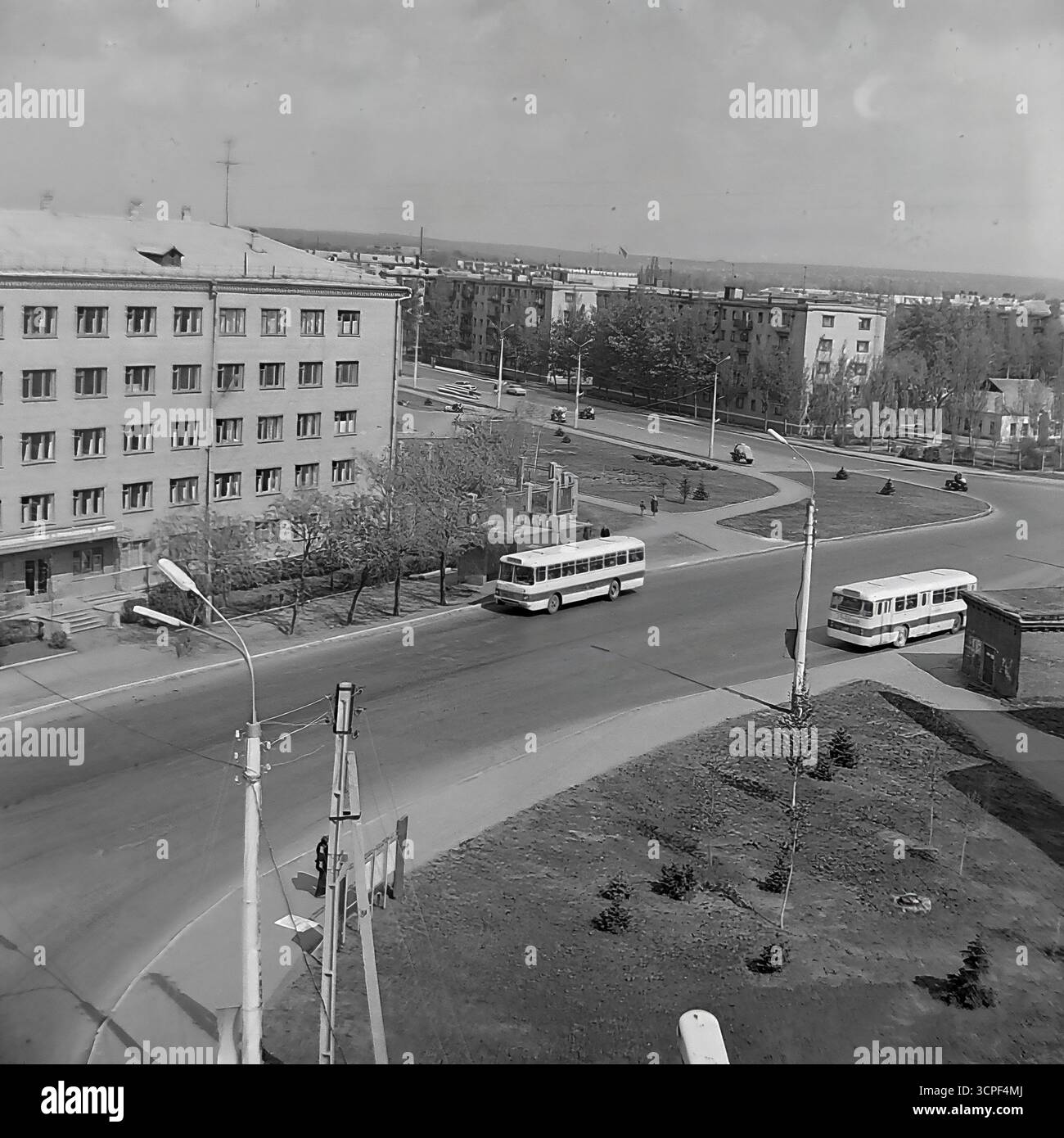 Deux bus classiques LAZ-695, un modèle emblématique des transports publics soviétiques, naviguent sur un large carrefour routier dans le quartier de l'École technique d'aviation (SATU) à Sloviansk, en RSS d'Ukraine, dans les années 1970 Cette photo d'archive monochrome, prise d'un point de vue élevé, capture un paysage urbain typique de l'époque, mettant en valeur l'infrastructure de la ville et le flux quotidien de la circulation sur fond de bâtiments standard de style soviétique. Banque D'Images