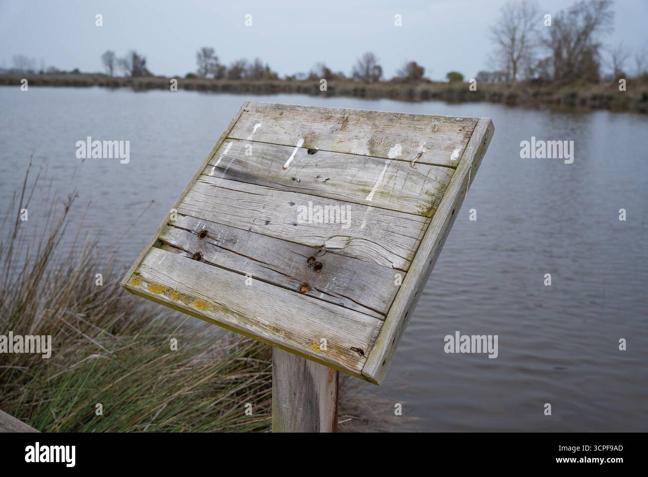 Panneau de signalisation en bois vierge altéré par un lac calme ou une zone humide le jour d'automne Banque D'Images