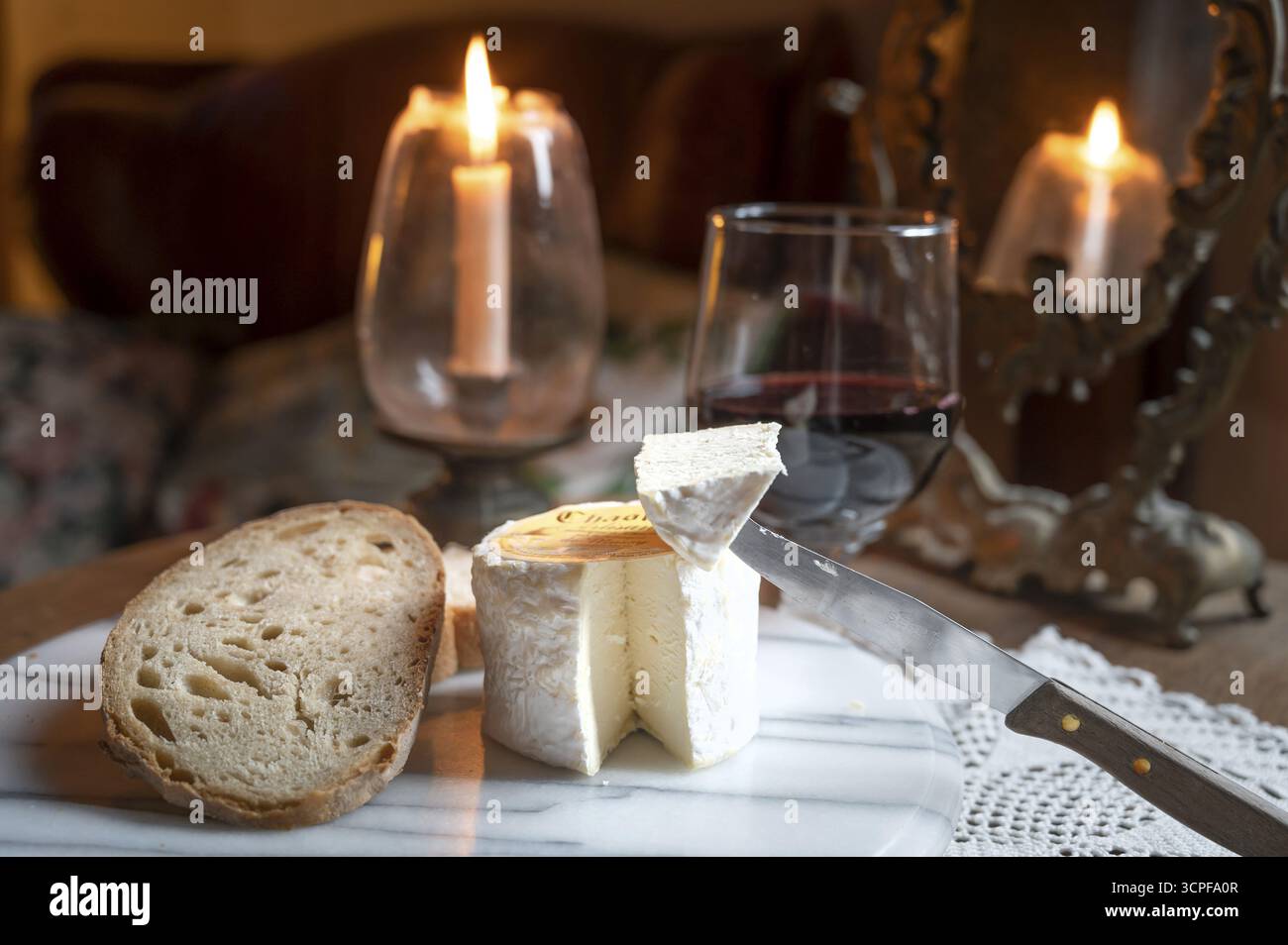 Le fromage Chaource présenté en tranches avec du pain et du vin rouge à la lueur chaude des chandelles, typique de la Champagne, impressionne par son moisissure blanche moelleuse Banque D'Images