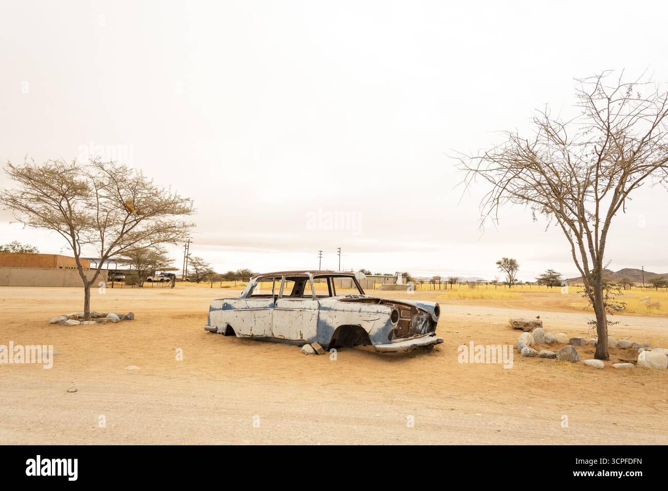 Le cimetière de voitures de Solitaire en Namibie présente des voitures anciennes rouillées près de petits bâtiments désertiques, situés contre des dunes et des montagnes, capturant le charme du désert Banque D'Images