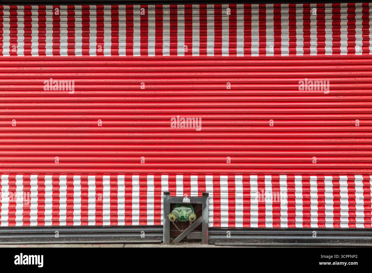 Bouche d'incendie verte devant un volet rouge à rayures blanches Banque D'Images