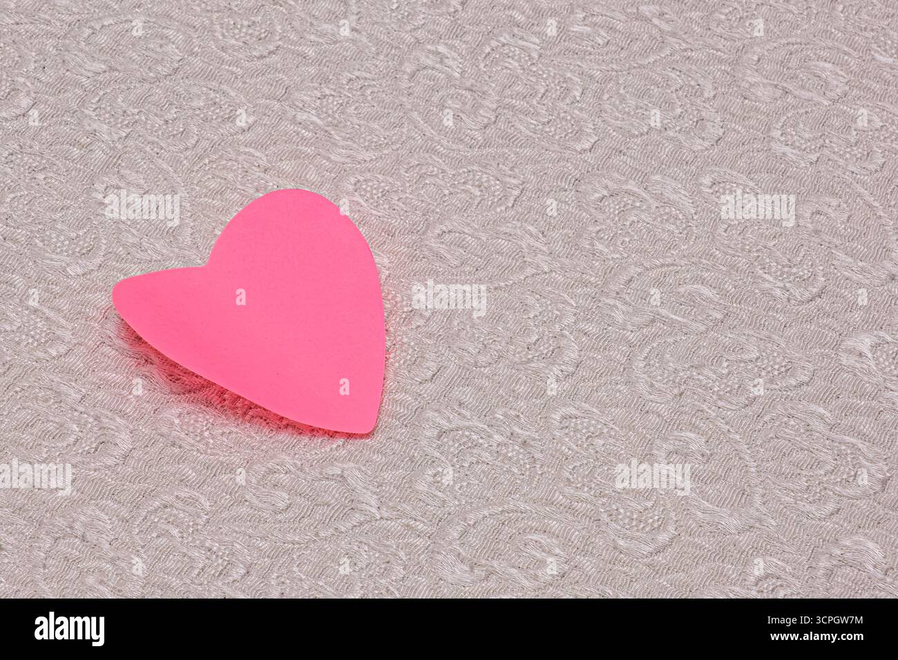 Un coeur rose est sur un tapis blanc. Le cœur est fait de papier et est de couleur rose. Banque D'Images