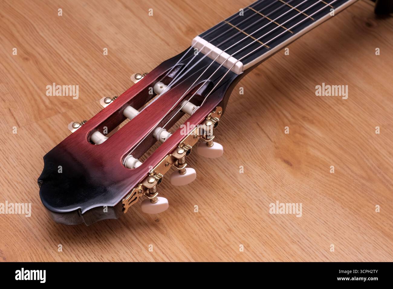 Une guitare avec une poupée noire et rouge repose sur une surface en bois. La poupée est ornée de quincaillerie en or et la guitare est un modèle vintage Banque D'Images