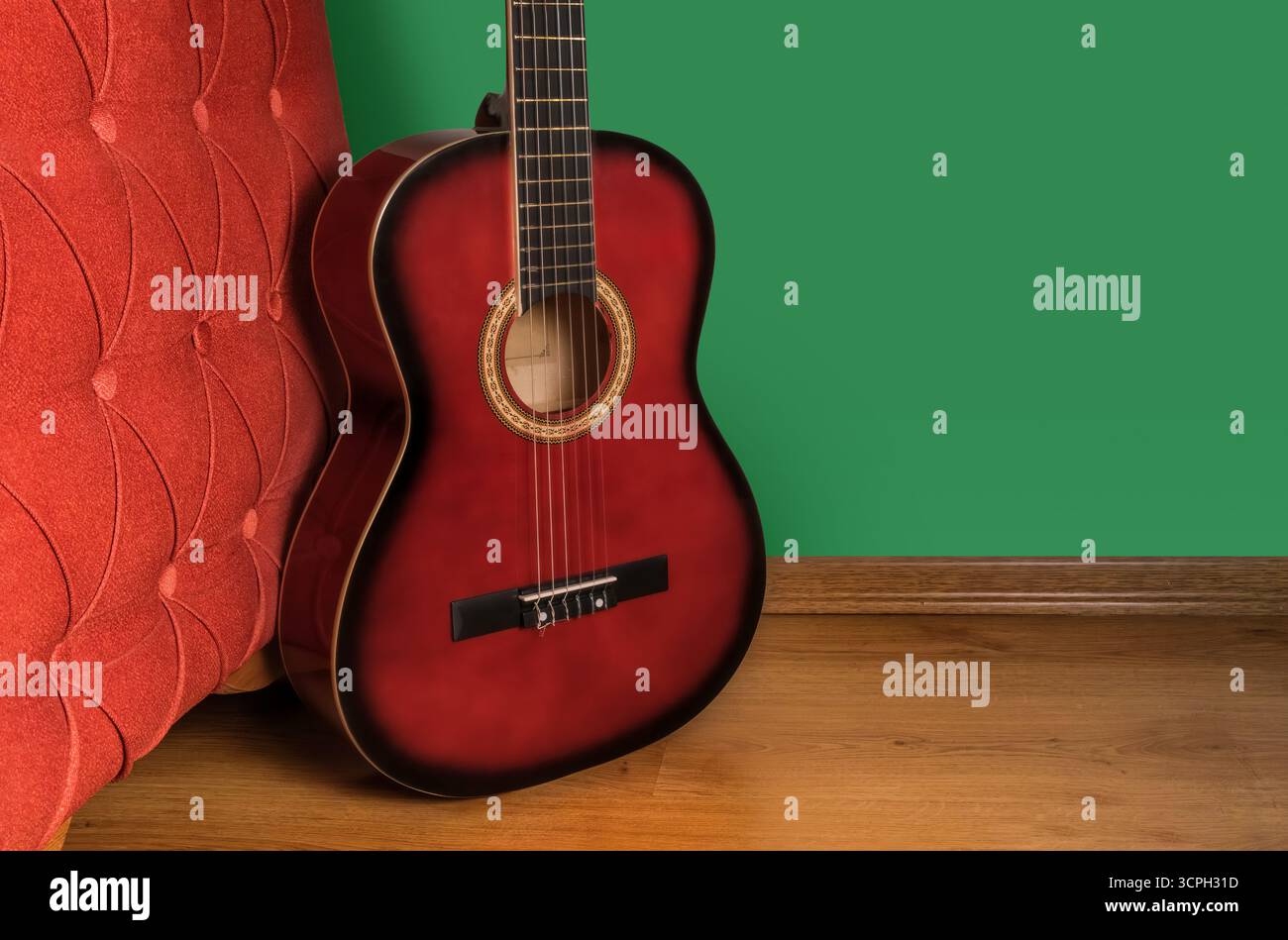 Une guitare rouge est assise sur un plancher de bois à côté d'un mur vert. La guitare est le centre principal de l'image, et c'est un modèle vintage Banque D'Images
