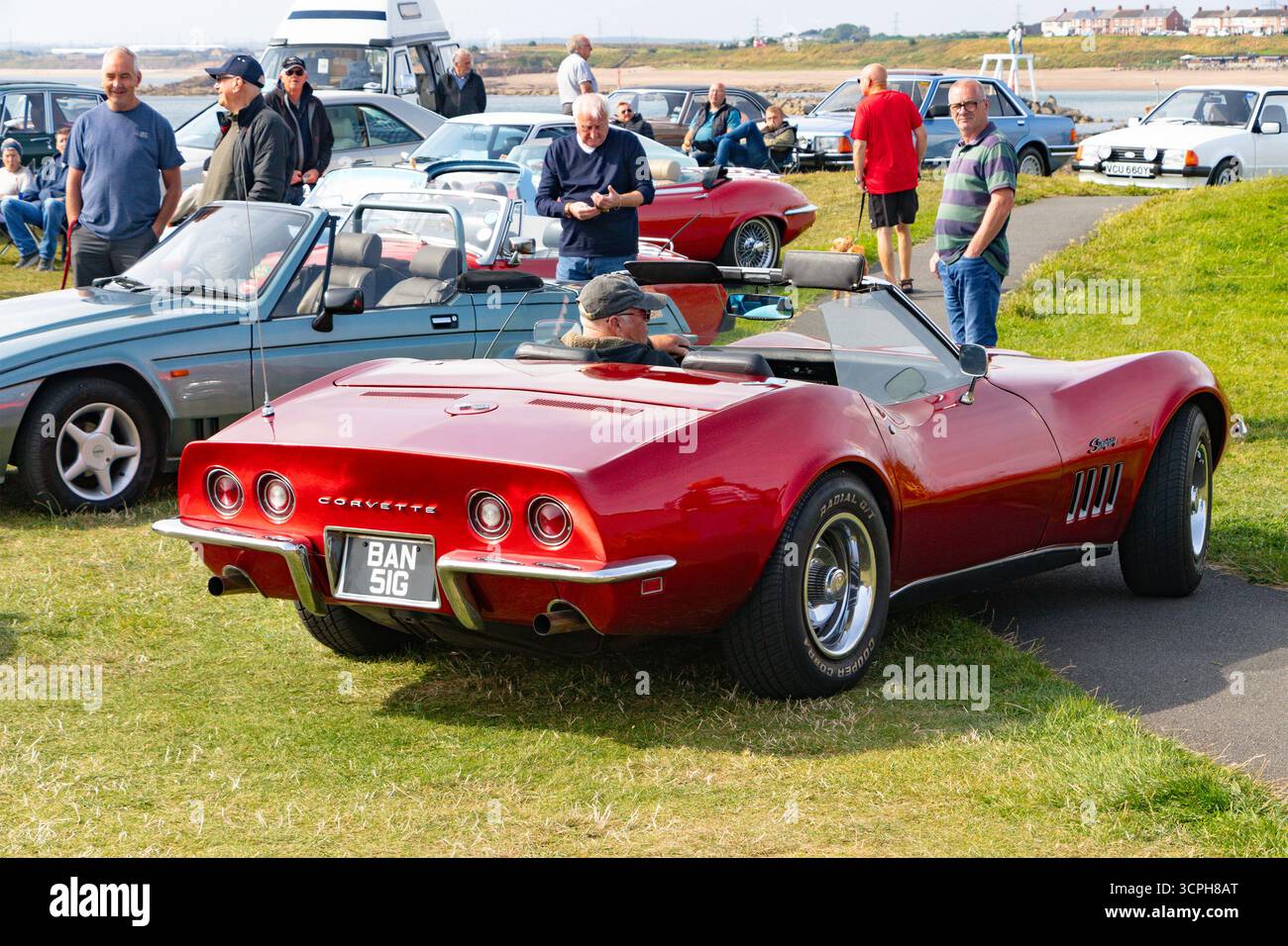 Les gens se rassemblent à un salon de voitures anciennes mettant en vedette une Corvette rouge cabriolet et diverses voitures anciennes par une journée ensoleillée Banque D'Images
