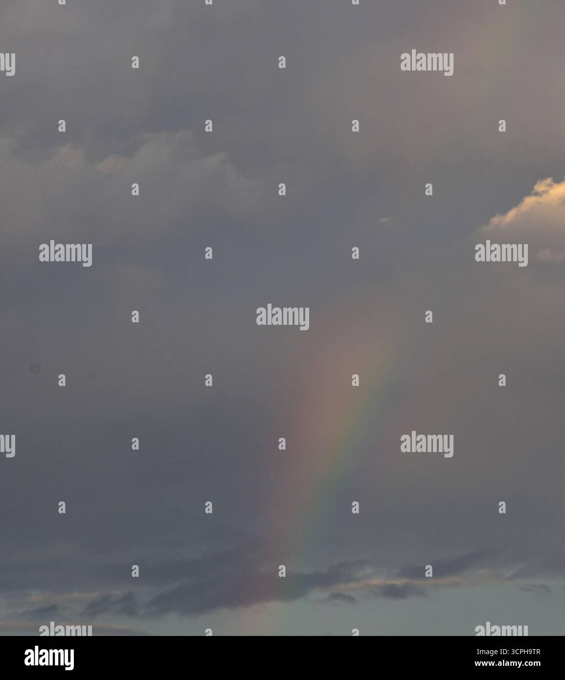 Un arc-en-ciel mystique brille à travers des nuages d'humeur, créant un moment surréaliste de lumière et de couleur dans le ciel naturel. Banque D'Images