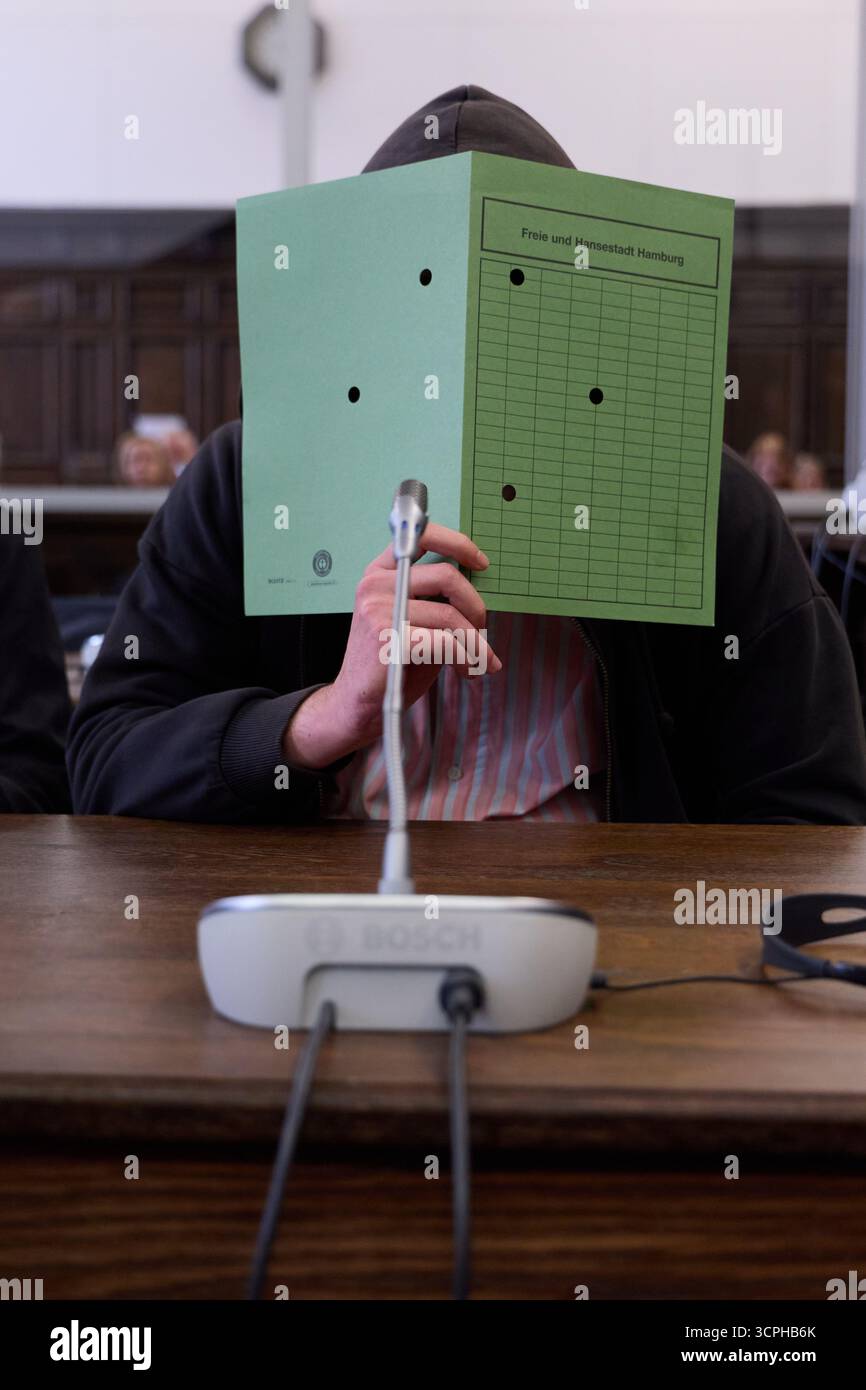 Hambourg, Allemagne. 26 septembre 2025. L'accusé couvre son visage dans la salle d'audience du bâtiment de la justice pénale. Le jeune homme de 25 ans attend la condamnation dans le cadre de la procédure préliminaire contre lui pour homicide involontaire de sa mère et tentative de meurtre de sa belle-mère. L'accusé aurait tué sa mère biologique avec plusieurs coups de couteau dans l'appartement qu'ils partageaient en février 2025. Crédit : Georg Wendt/dpa/Alamy Live News Banque D'Images