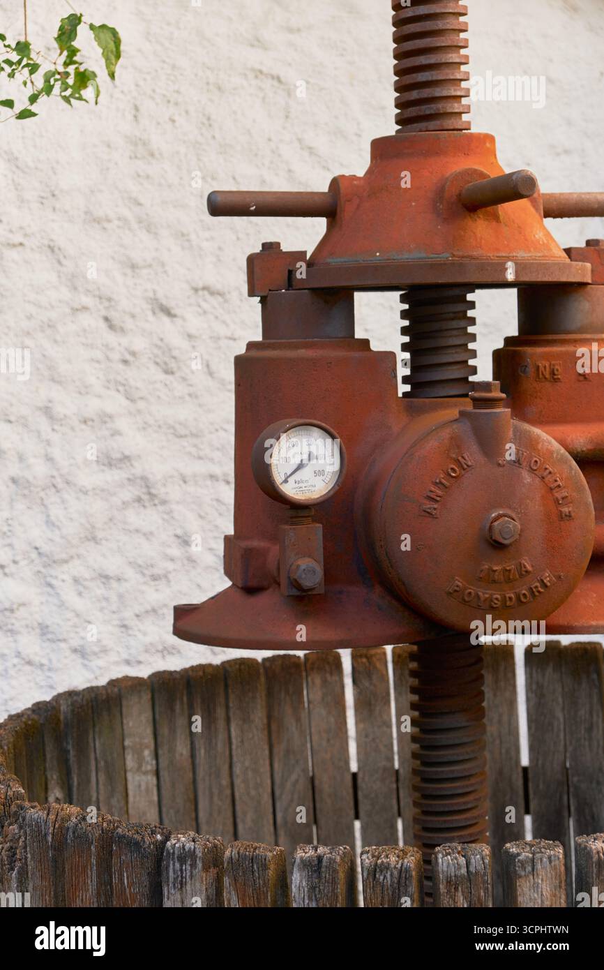 Gros plan du pressoir à vin en métal rouillé dans un tonneau en bois avec des roues en métal vert. Matériel historique de vinification, artisanat vintage, photographié Banque D'Images