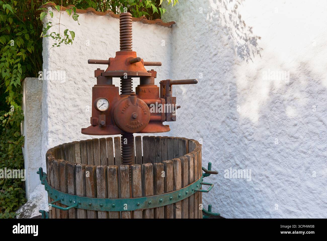 Pressoir à vin antique rouillé dans un tonneau en bois avec des roues en métal vert, photographié légèrement de loin. Matériel historique de vinification en rustique, sce Banque D'Images