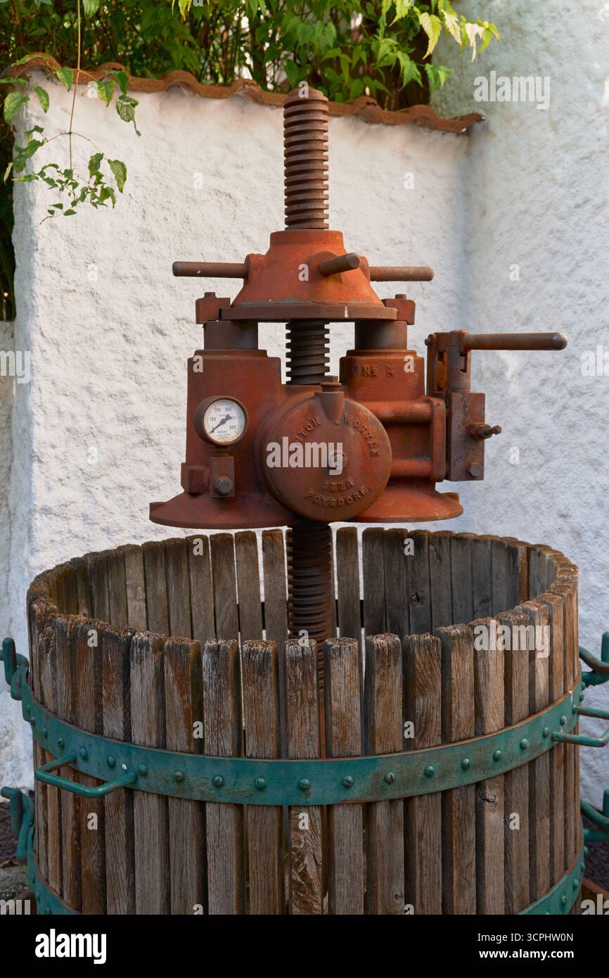 Pressoir à vin en métal rouillé historique dans un tonneau en bois avec des roues vertes, vu d'une petite distance. Équipement de cave vintage classique, photographié outd Banque D'Images