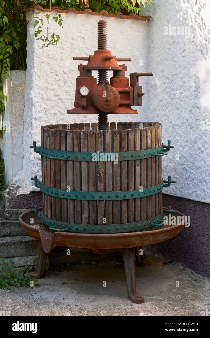 Presse à vin en métal rouillé dans un tonneau en bois avec des roues vertes, photographié à l'extérieur. Outil de vinification historique au charme vintage, mettant en valeur les artisans Banque D'Images