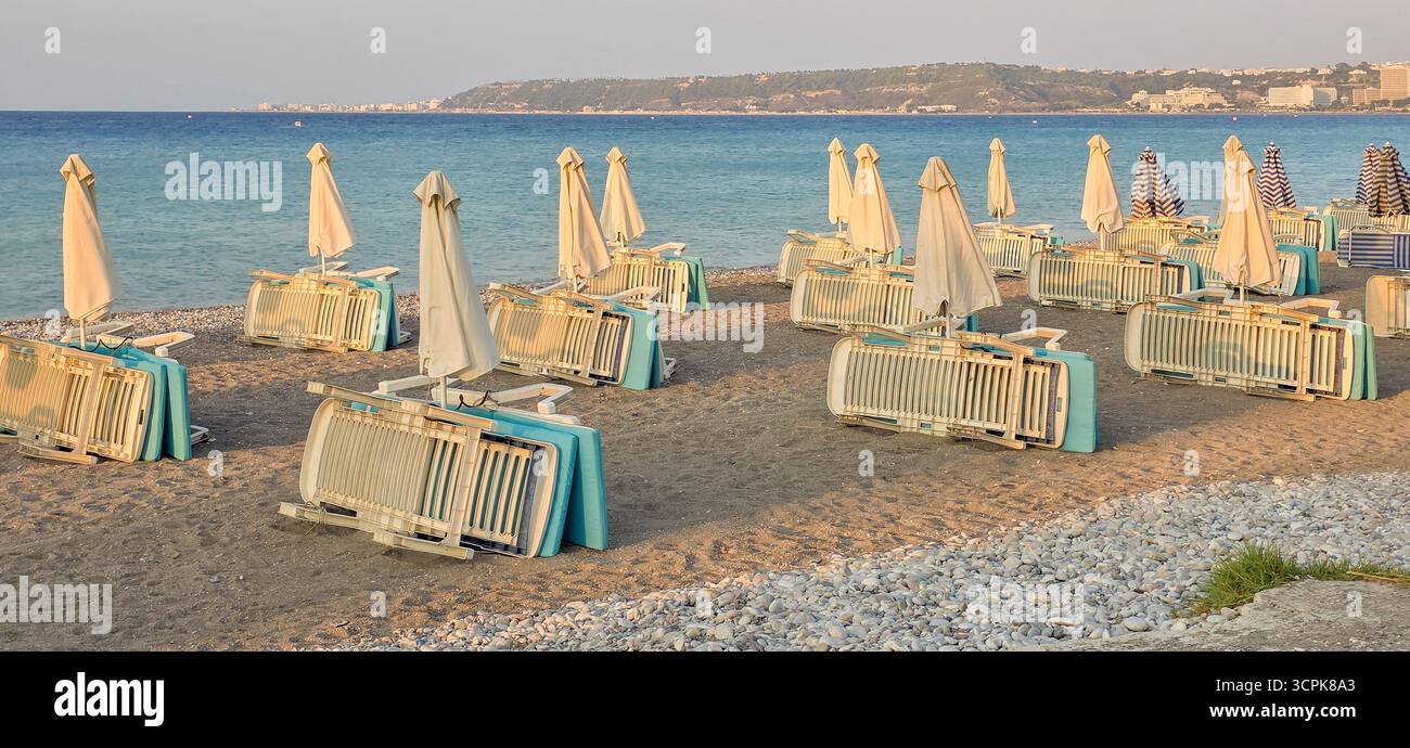 Des chaises longues vides et des parasols pliés bordent un rivage de sable, au bord d'une mer calme Banque D'Images