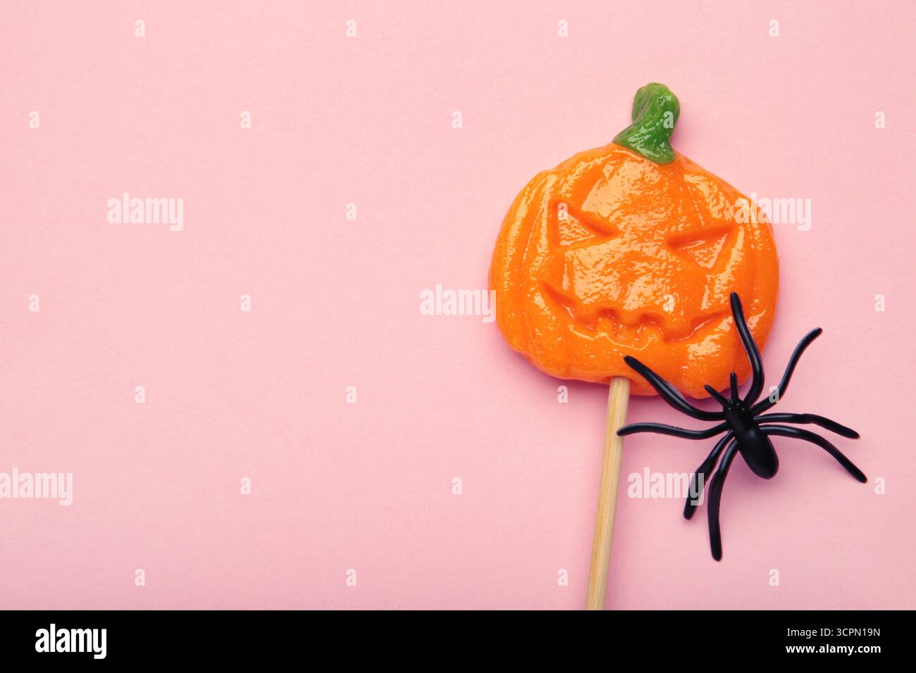 Sucettes d'Halloween en forme de citrouille avec araignée décorative sur fond rose. Espace pour espace. Vue de dessus Banque D'Images