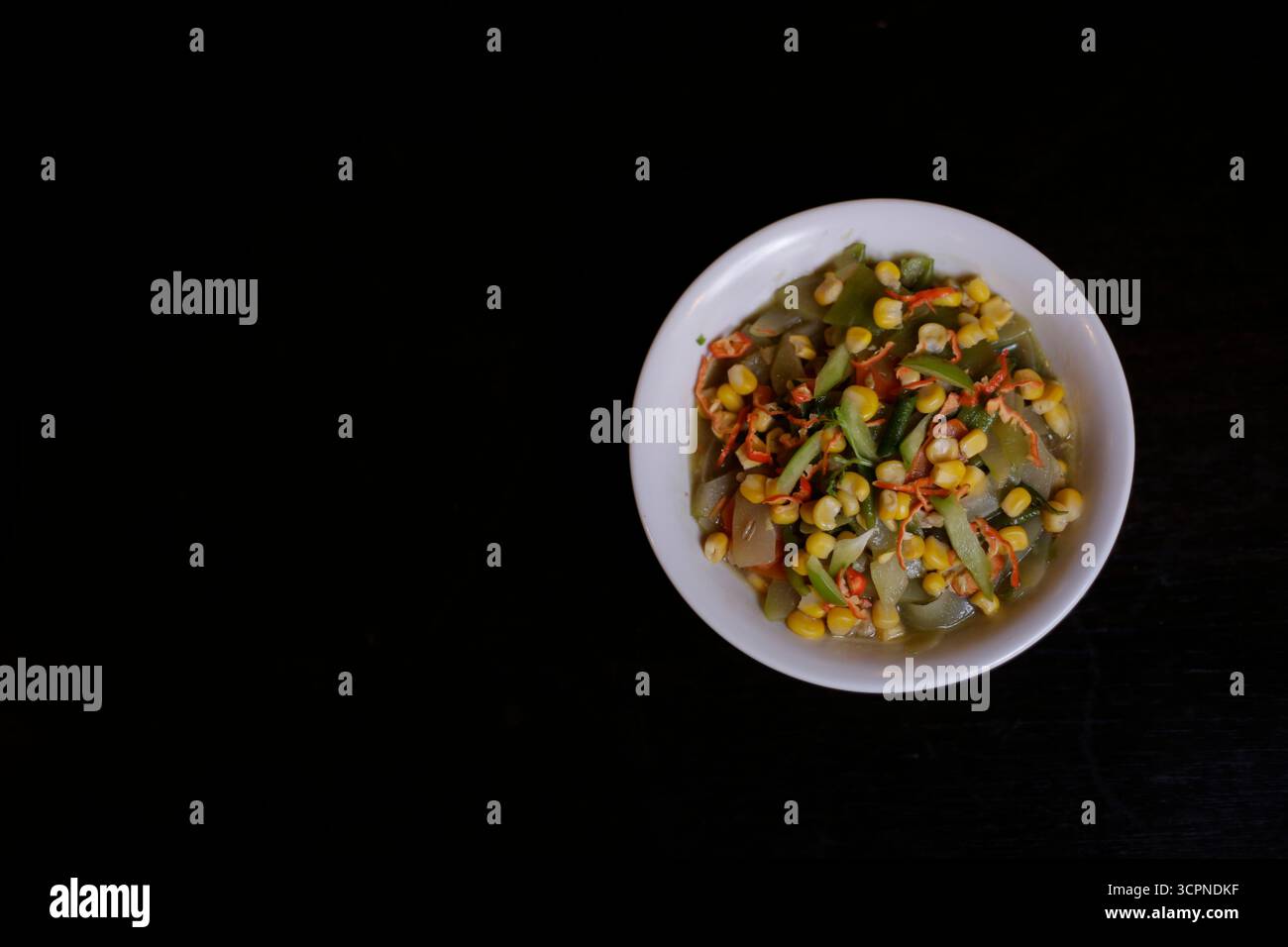 Légumes mélangés sautés avec du maïs dans un bol blanc sur fond noir Banque D'Images