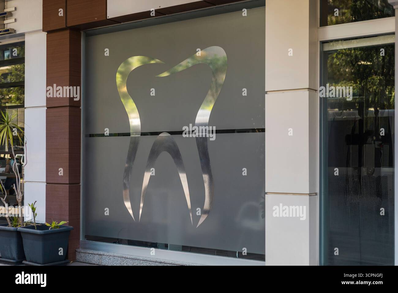 Un grand symbole de dent est affiché sur une fenêtre en verre dépoli d'une clinique dentaire dans une ville animée. La lumière du soleil illumine les environs Banque D'Images