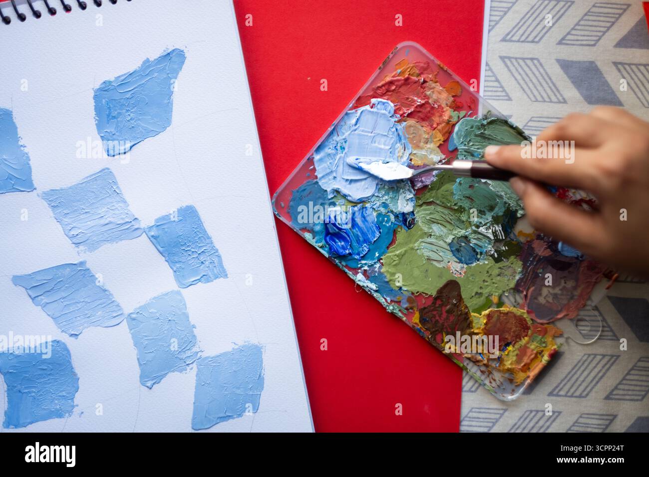 Artiste travaillant avec couteau à palette et couleurs acryliques, créant des échantillons texturés sur carnet de croquis, fond artistique Banque D'Images