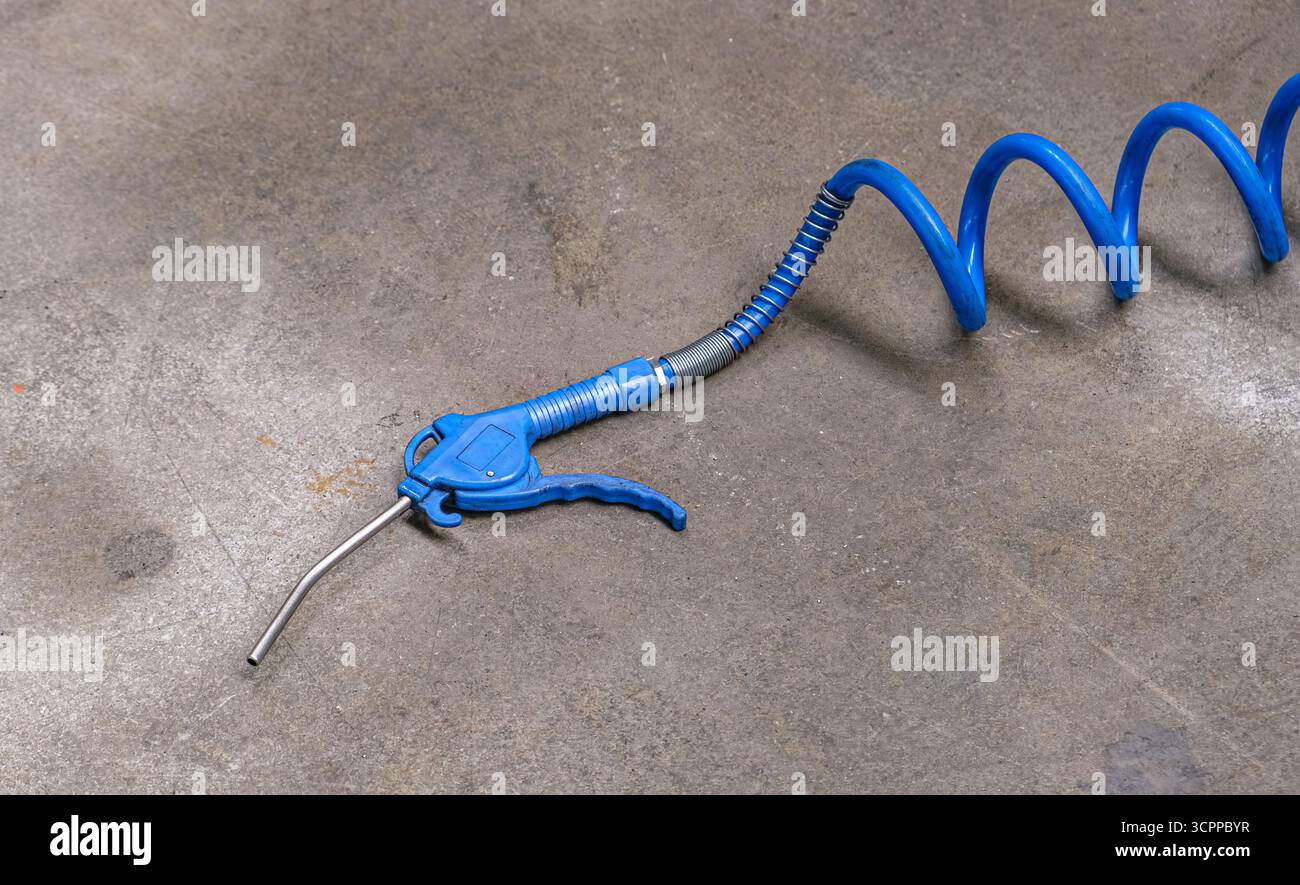 Pistolet de compresseur d'air industriel avec tuyau enroulé sur sol en béton. Burin pneumatique à marteau pneumatique, régule le débit d'air du compresseur. Banque D'Images