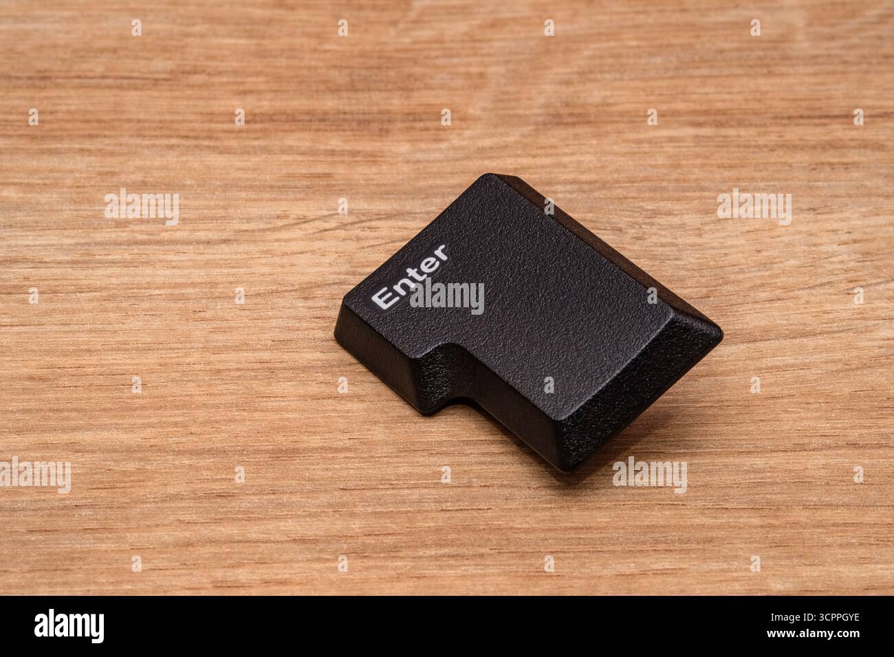 Touche entrée. Touche 'entrée' détachée d'un clavier, placée sur une surface en bois. La clé montre sa surface texturée et sa forme en l distinctive. Banque D'Images