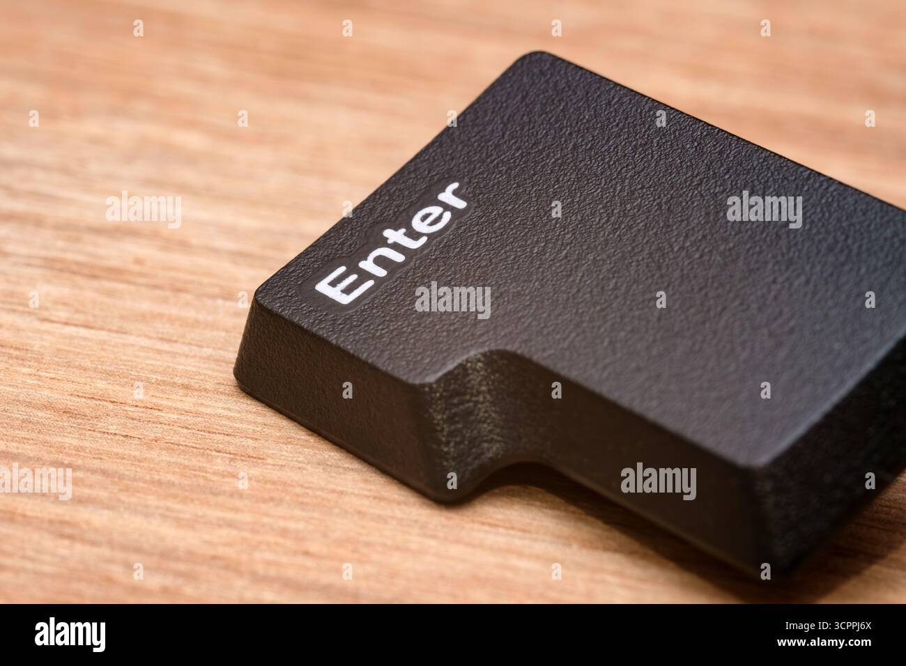 Photographie macro de la touche entrée noire détachée d'un clavier d'ordinateur, placée sur une surface en bois. Idéal pour une utilisation éditoriale, blogs technologiques. Banque D'Images