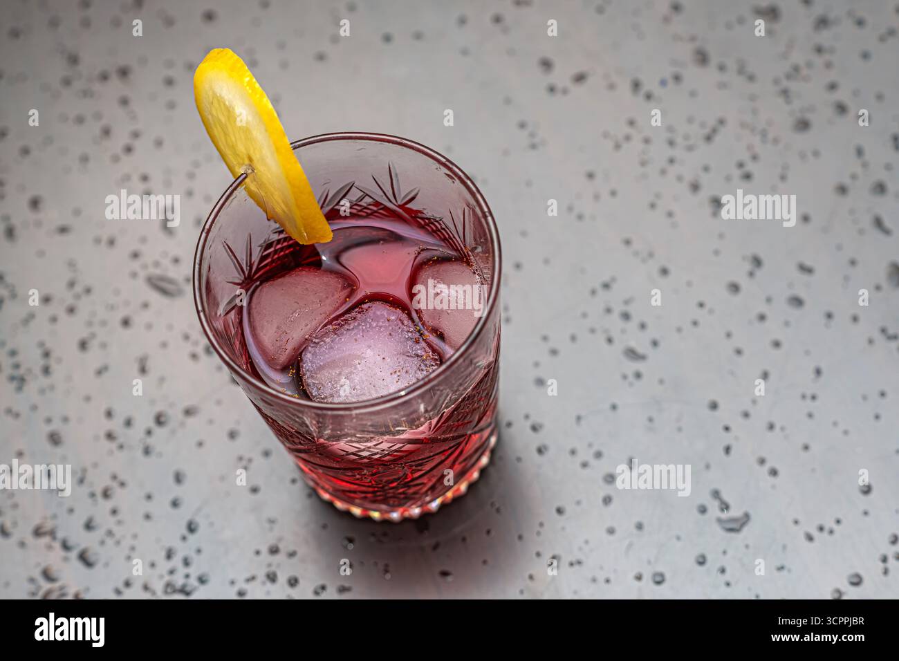 Cocktail rouge rafraîchissant avec glace et garniture de citron. Gros plan d'un cocktail rouge rafraîchissant servi dans un verre de cristal vintage. Mise au point sélective. Banque D'Images