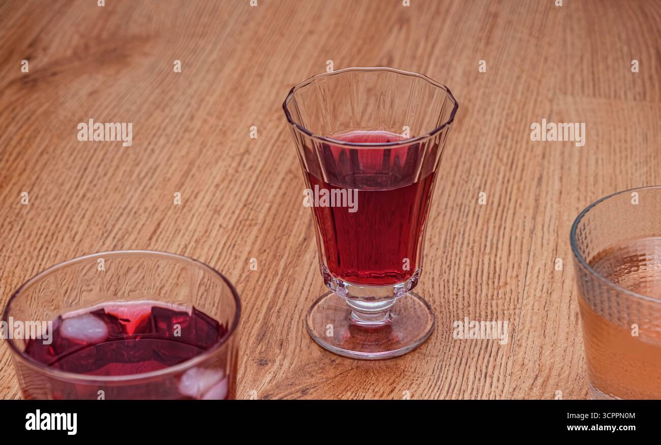 Une boisson froide et rouge foncé servie dans un grand. Verre transparent avec glaçons. Parfait pour une journée chaude ou comme accompagnement rafraîchissant aux repas. Caler contre le bois. Banque D'Images