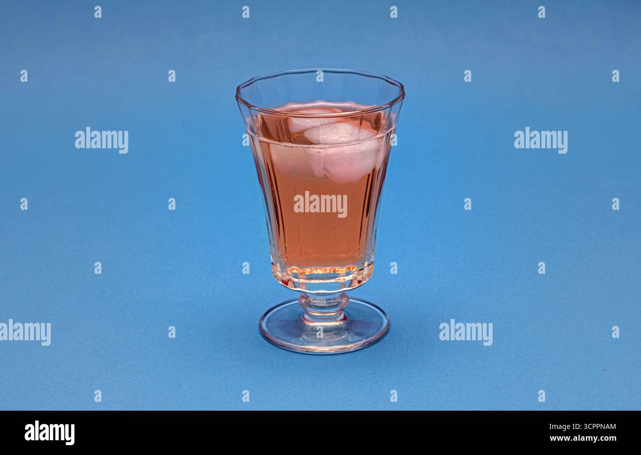 Un verre élégant rempli d'une boisson repose sur un fond bleu. Cette image est idéale pour le marketing de boissons, les recettes de cocktails ou le contenu de style de vie. Banque D'Images