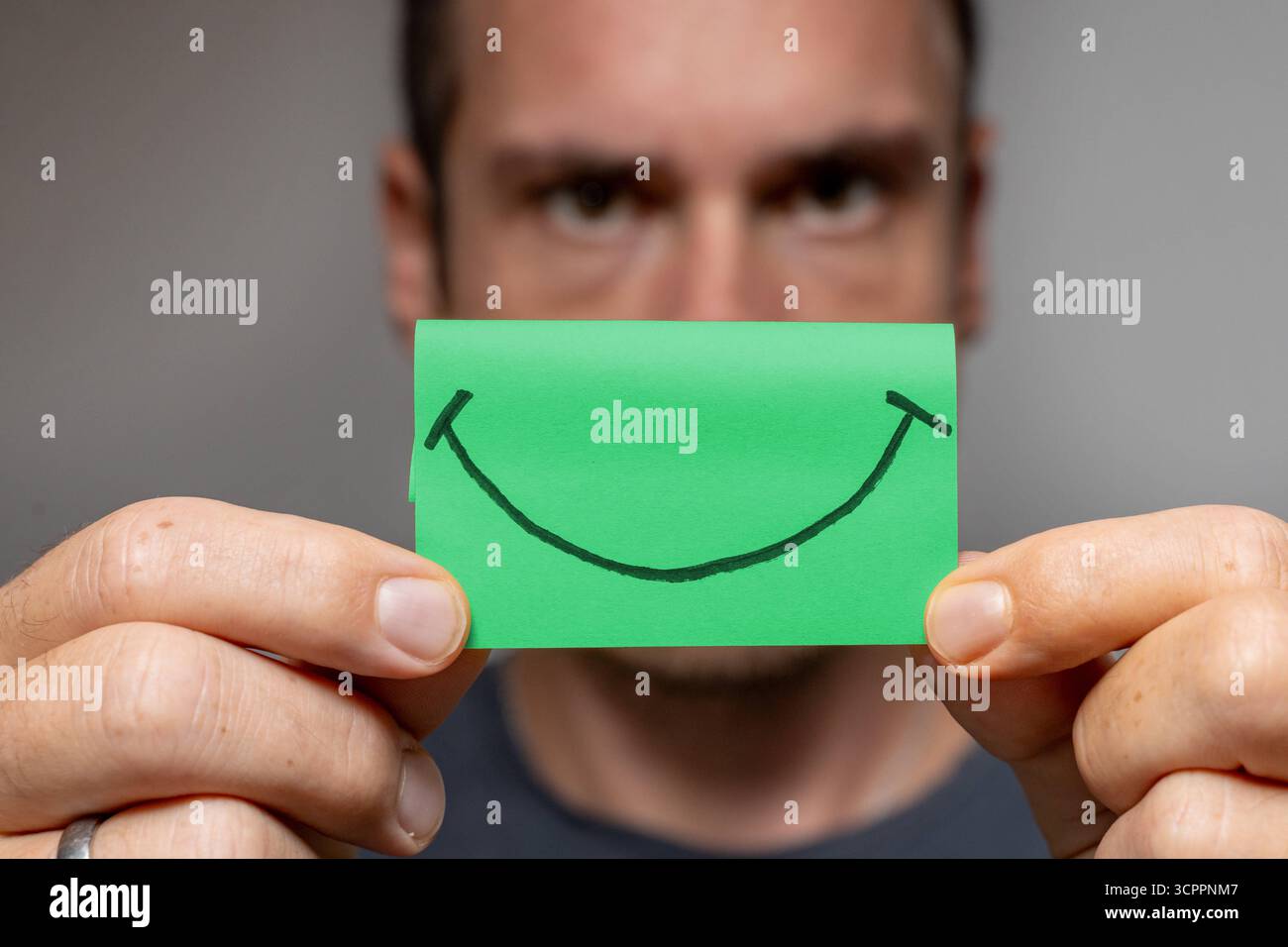 Allemagne - 27 septembre 2025 : un homme tient un Post-it vert avec un visage souriant, symbole de bonheur, de joie et d'optimisme. *** Mann hält ein Grünes Post-it mit einem lächelnden Smiley vor sich Symbol für Glück, Freude und Optimismus. Banque D'Images