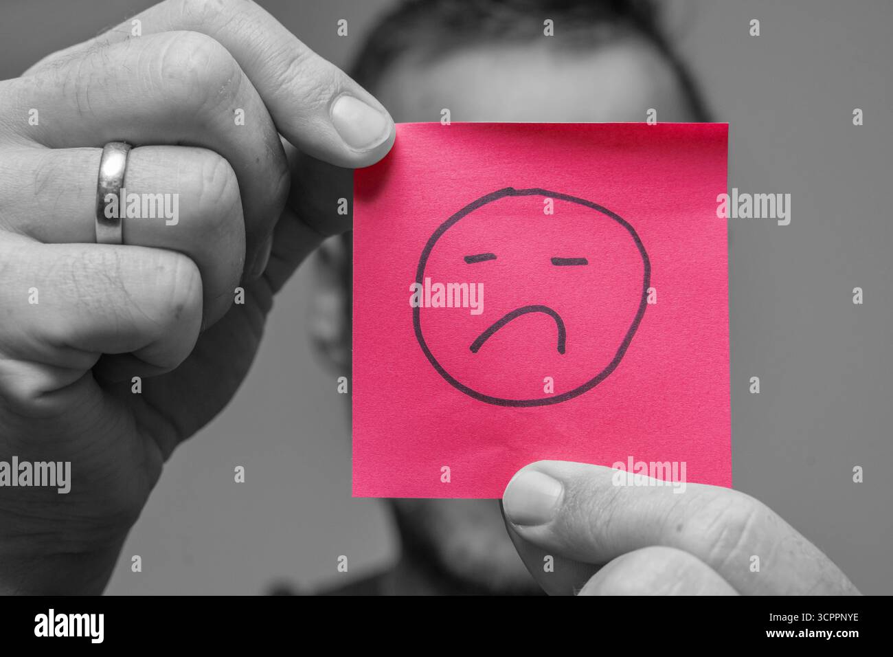 Allemagne - 27 septembre 2025 : un homme tient un morceau de papier avec un triste symbole dessus. L'image symbolise l'humeur dépressive de nombreuses personnes en raison des crises actuelles telles que la pandémie, la guerre en Ukraine, la menace de guerre et l'inflation en Allemagne. Il représente l'insatisfaction dans la vie quotidienne ou au travail et illustre la frustration, la surcharge et un manque de contentement. *** Ein Mann hält ein Zettelchen mit traurigem symbole vor sich. DAS Bild symbolisiert die gedrückte Stimmung vieler Menschen durch aktuelle Krisen wie Pandemie, Krieg in der Urkaine und Kriegsgefahr und inflation in Deutschla Banque D'Images