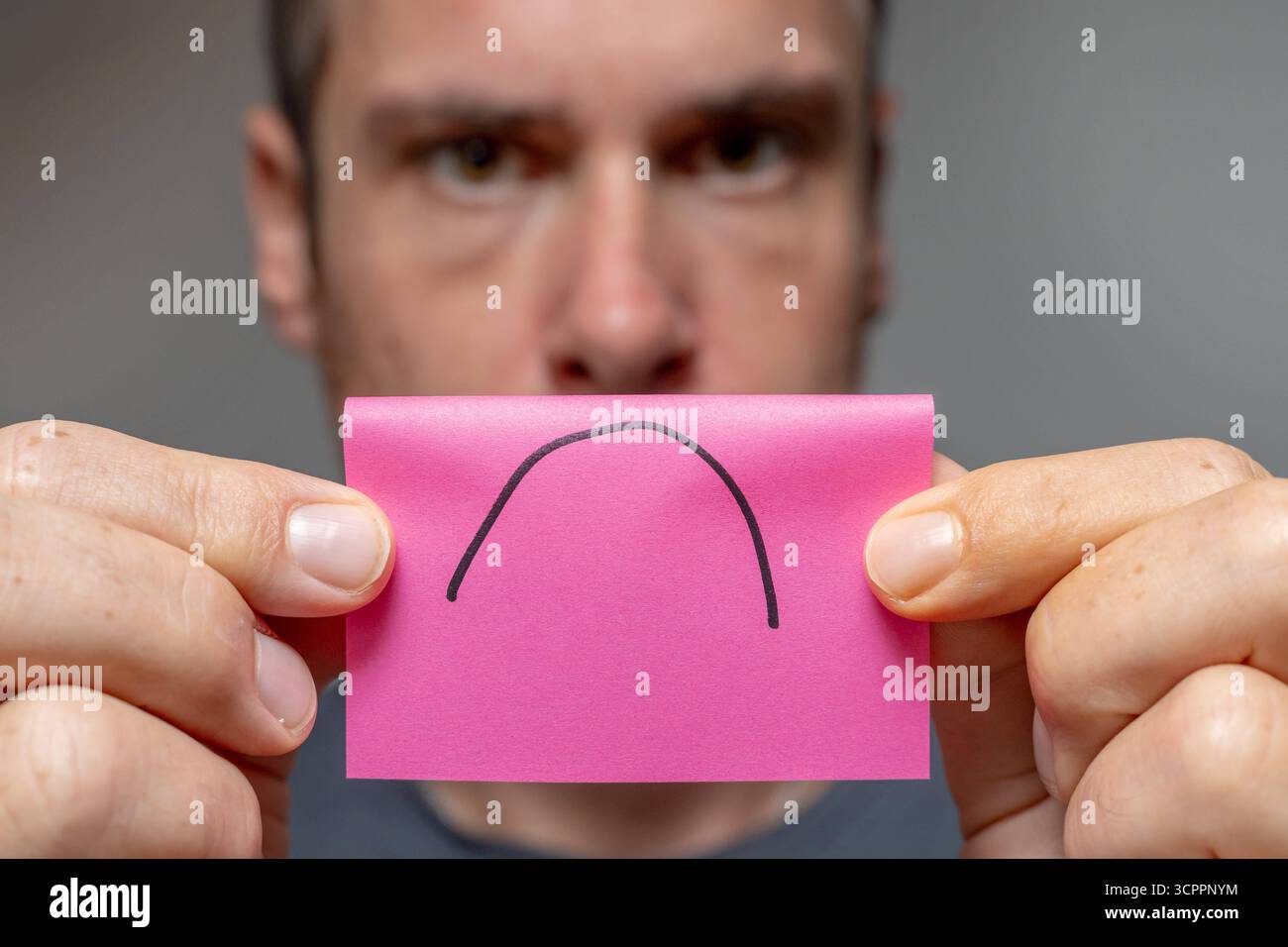 Allemagne - 27 septembre 2025 : un homme tient un morceau de papier avec un triste symbole dessus. L'image symbolise l'humeur dépressive de nombreuses personnes en raison des crises actuelles telles que la pandémie, la guerre en Ukraine, la menace de guerre et l'inflation en Allemagne. Il représente l'insatisfaction dans la vie quotidienne ou au travail et illustre la frustration, la surcharge et un manque de contentement. *** Ein Mann hält ein Zettelchen mit traurigem symbole vor sich. DAS Bild symbolisiert die gedrückte Stimmung vieler Menschen durch aktuelle Krisen wie Pandemie, Krieg in der Urkaine und Kriegsgefahr und inflation in Deutschla Banque D'Images