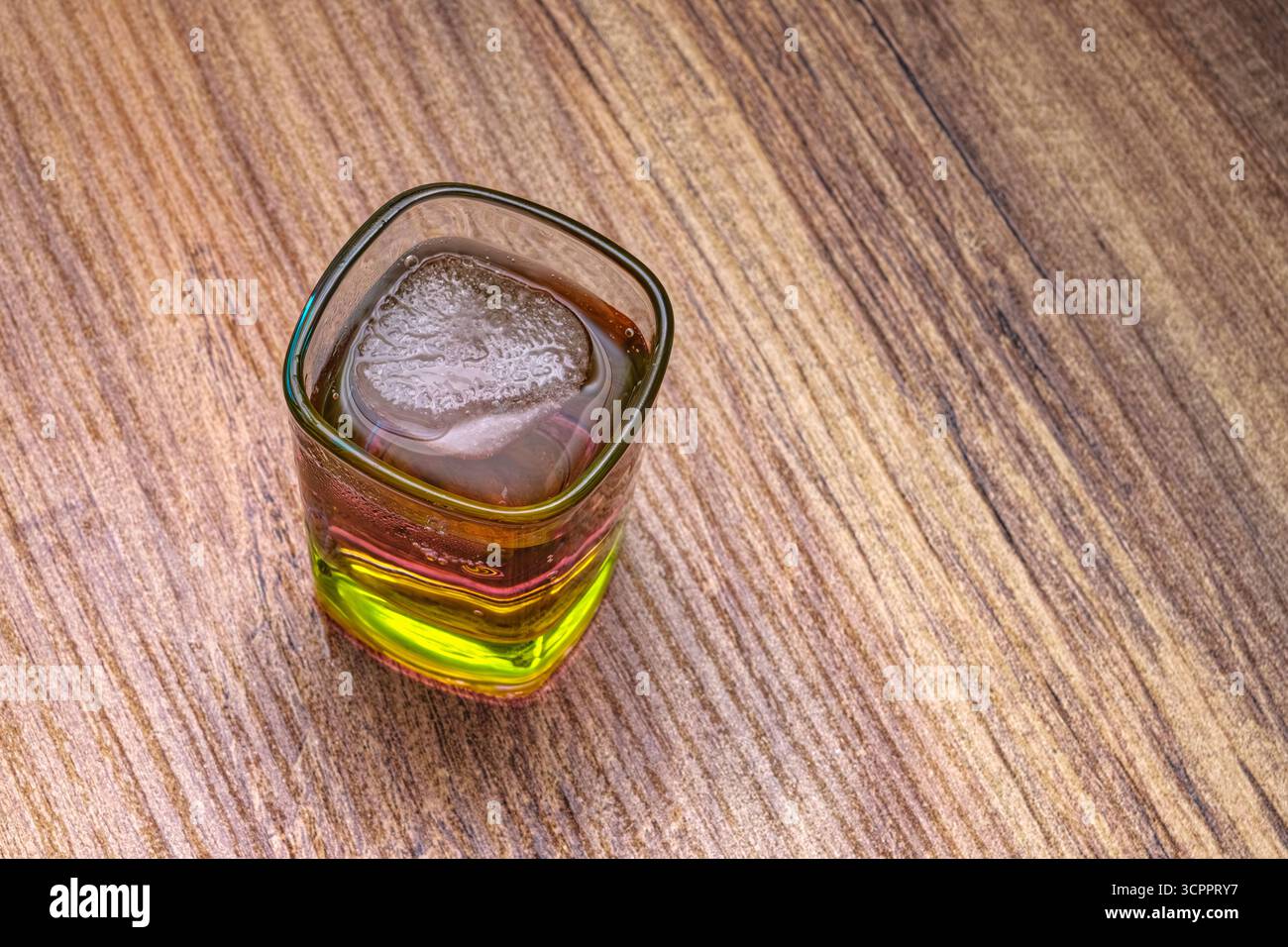 Le cocktail aux teintes vertes et brunes vibrantes avec des glaçons sur une table en bois. La boisson crée un effet captivant. Banque D'Images