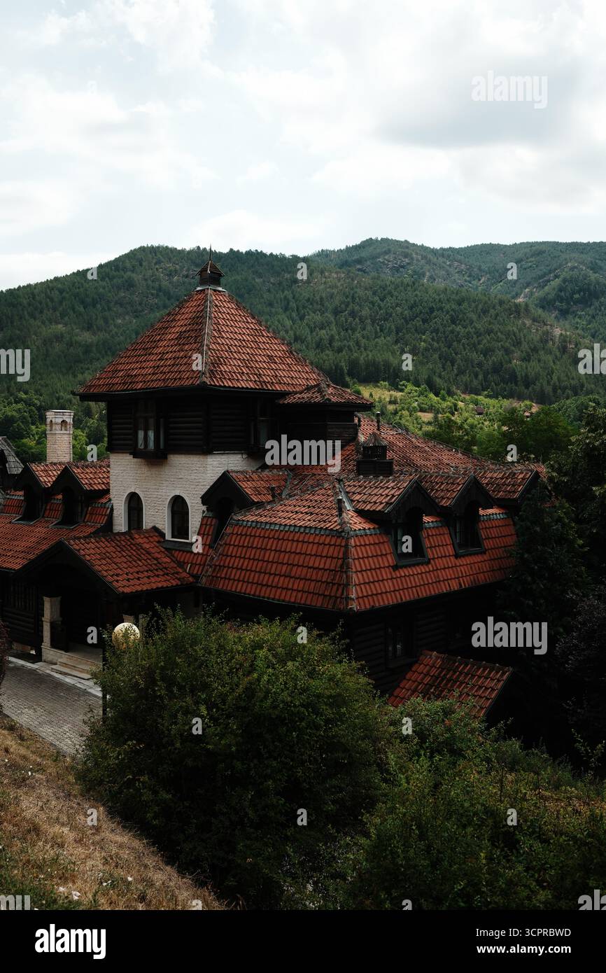 Grande maison traditionnelle avec toit de tuiles rouges à Mokra Gora, en Serbie, entourée de collines boisées. Banque D'Images