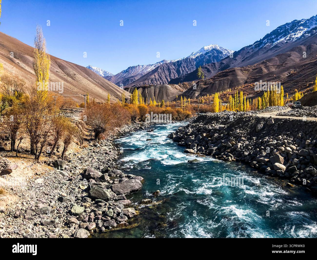 Une rivière glaciaire serpente sous les puissants sommets du Karakoram, encadrés par les teintes dorées de l'automne Banque D'Images