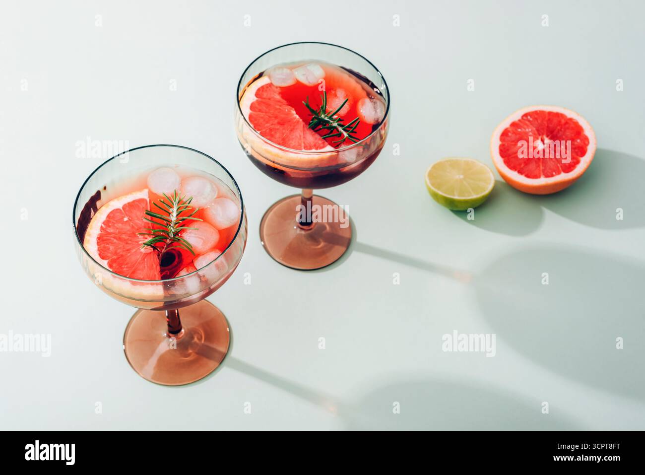 Deux cocktails rafraîchissants avec tranches de pamplemousse, glaçons, romarin et citron vert sur fond clair, concept de boisson estivale. Banque D'Images
