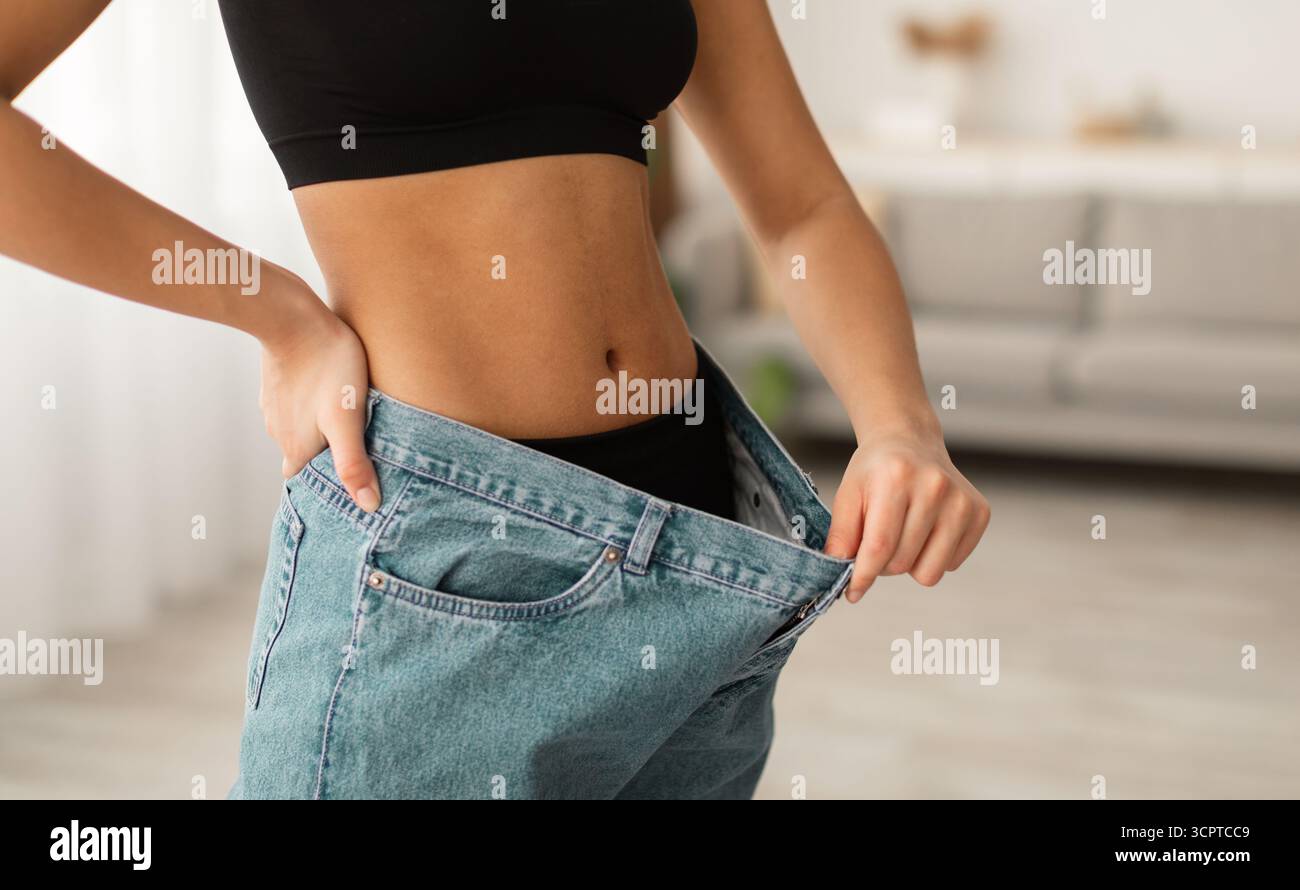 Une dame noire non reconnaissable montrant des muscles abdominaux portant des jeans surdimensionnés en intérieur Banque D'Images