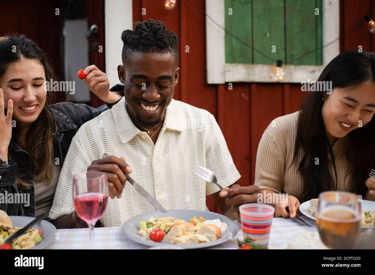Heureux jeune homme mangeant de la nourriture tout en étant assis avec des amis au dîner dans la cour arrière Banque D'Images