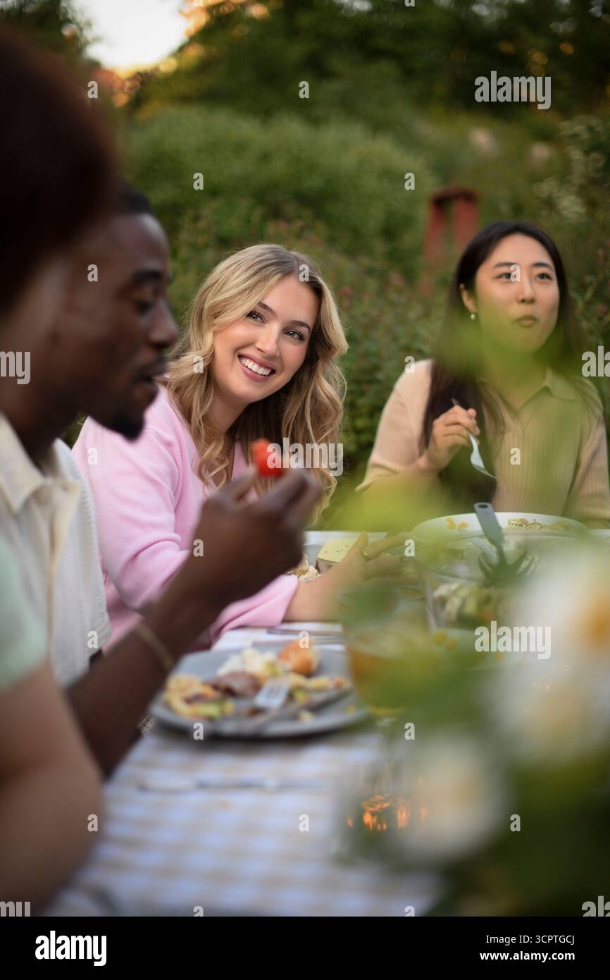 Femme blonde souriante assise avec des amis mangeant de la nourriture au dîner dans la cour arrière Banque D'Images