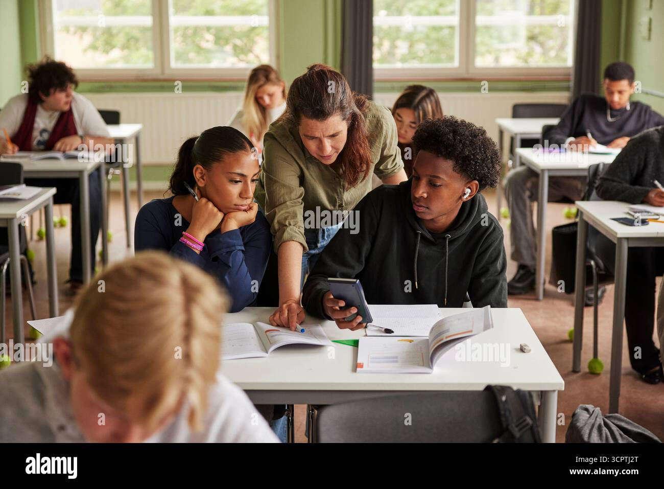 Enseignante aidant les élèves du premier cycle du secondaire à l'aide d'une calculatrice pour les problèmes de mathématiques en classe à l'école Banque D'Images