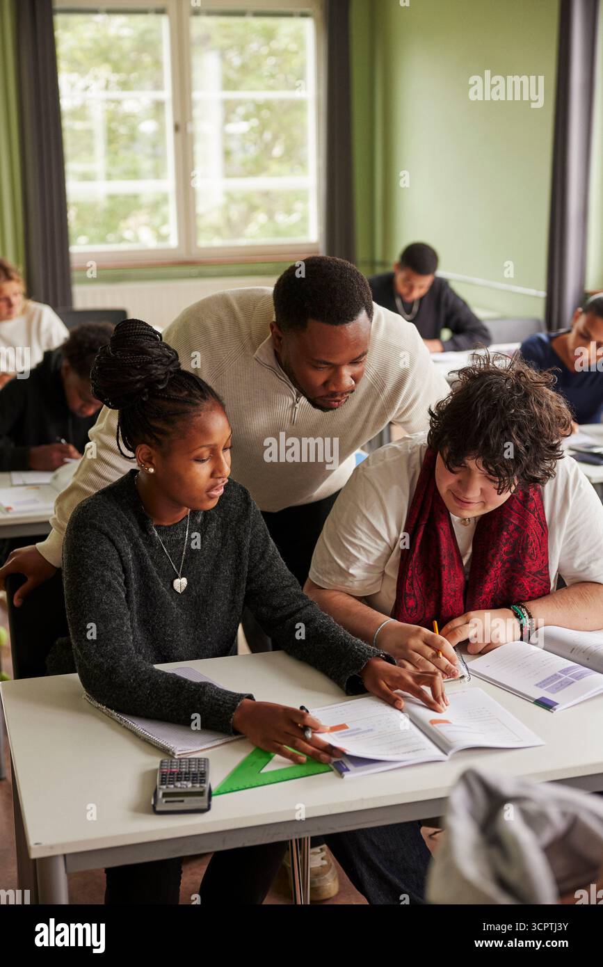Vue en angle élevé d'un enseignant masculin aidant les élèves à résoudre l'équation mathématique dans une classe secondaire Banque D'Images