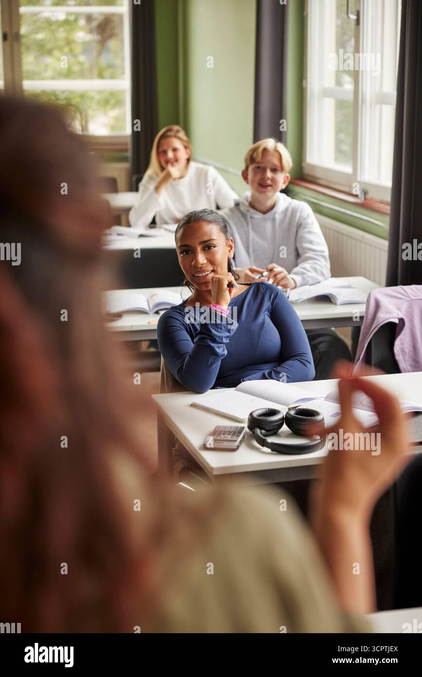 Portrait d'une adolescente souriante écoutant l'enseignant tout en étant assis dans la salle de classe assistant à la conférence à l'école Banque D'Images