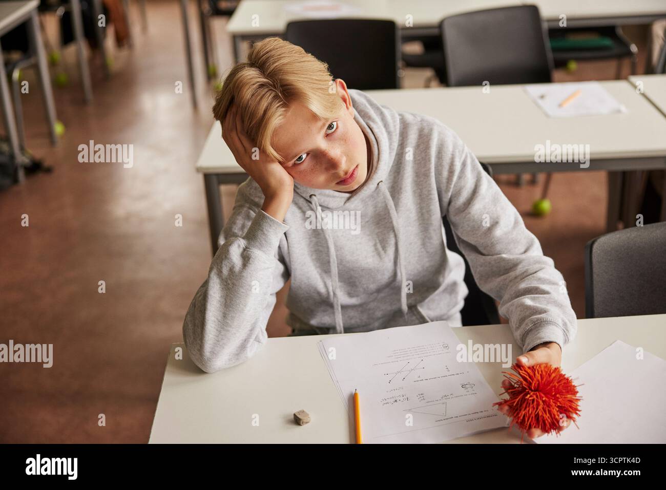 Portrait en angle élevé d'un adolescent de sexe masculin avec syndrome d'Asperger pressant balle de stress tout en étant assis dans la salle de classe à s. Banque D'Images