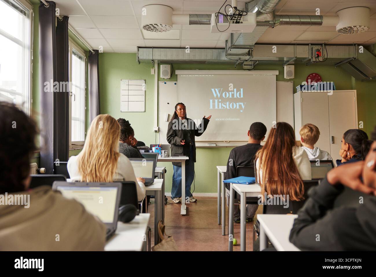 Professeur féminin enseignant sur l'histoire du monde sur l'écran de projection aux étudiants du secondaire en classe Banque D'Images