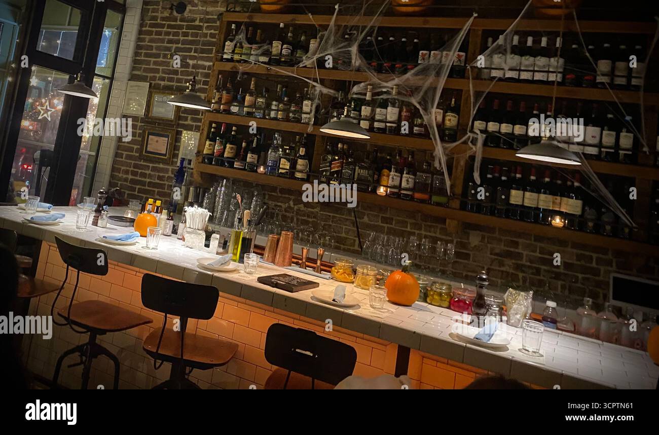 Bar décoré sur le thème de l'Halloween avec citrouilles, toiles d'araignée et bouteilles de vin sur des étagères murales en briques - Image de stock capturée avec un smartphone