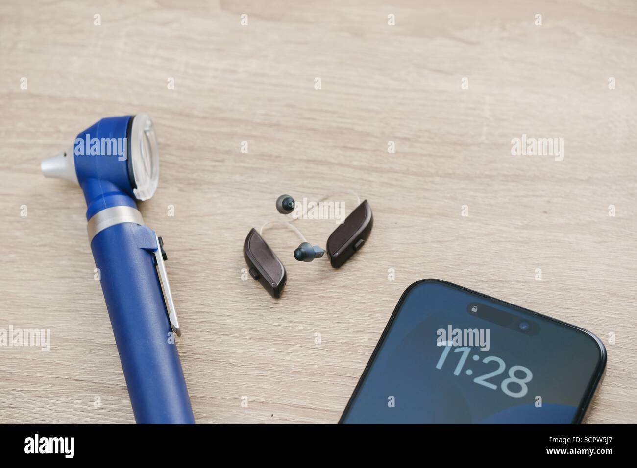 Vue de dessus minimaliste des aides auditives numériques modernes, otoscope et smartphone sur un bureau en bois. Mise en page propre en audiologie ou en contexte de soins auditifs. Copier Banque D'Images