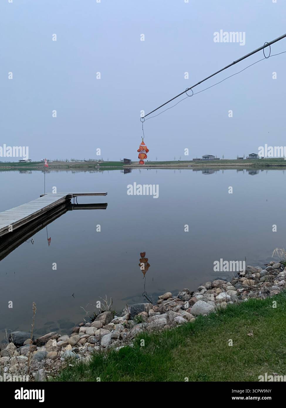 poisson hissé par un treuil sur un quai de pêche en bois s'étendant au-dessus du lac de prairie calme, horizon brumeux avec des cabanes. - Image de stock capturée avec un smartphone