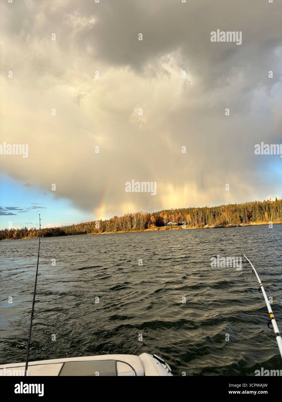 Arc-en-ciel au-dessus d'un lac du nord avec des cannes à pêche, encadré par une forêt automnale et des nuages spectaculaires au lever du soleil. - Image de stock capturée avec un smartphone