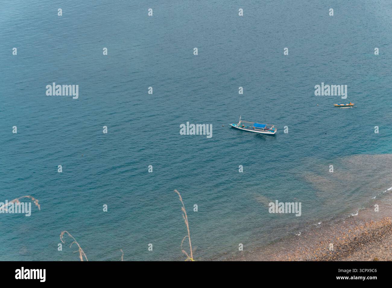 Vue en angle élevé d'un bateau de pêche traditionnel et d'un bateau plus petit flottant sur une eau bleu profond calme. Rivage rocheux et mer claire peu profonde dans le forterrou Banque D'Images